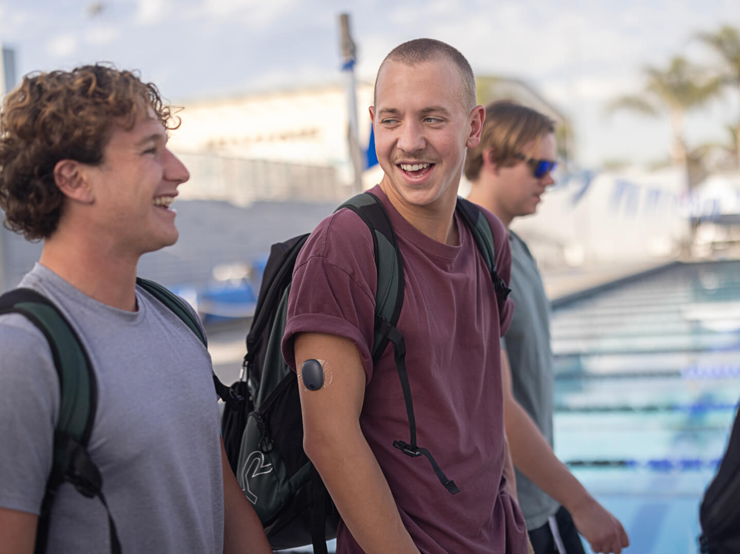 Two young men with backpacks smile - One wearing the Eversense removable smart transmitter on arm